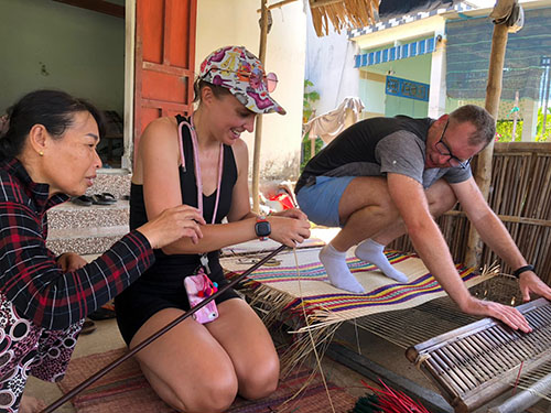 Two travelers learning how to weave Vietnamese mats