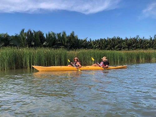 two women on a yellow kayak rowing by tall grass