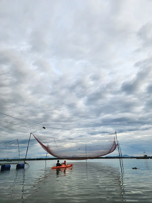 Two kayakers rowing under a red fishing net