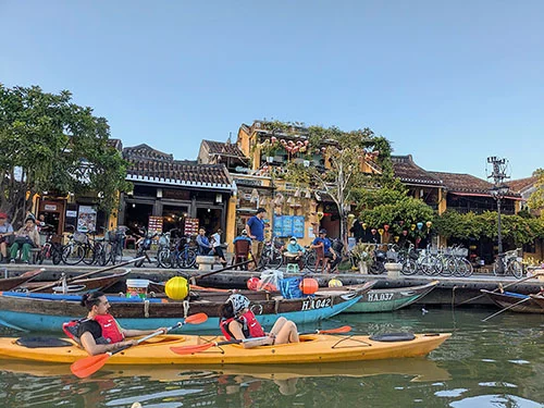 Two young women on their yellow kayak passing by the docks in the historic area of Hoian