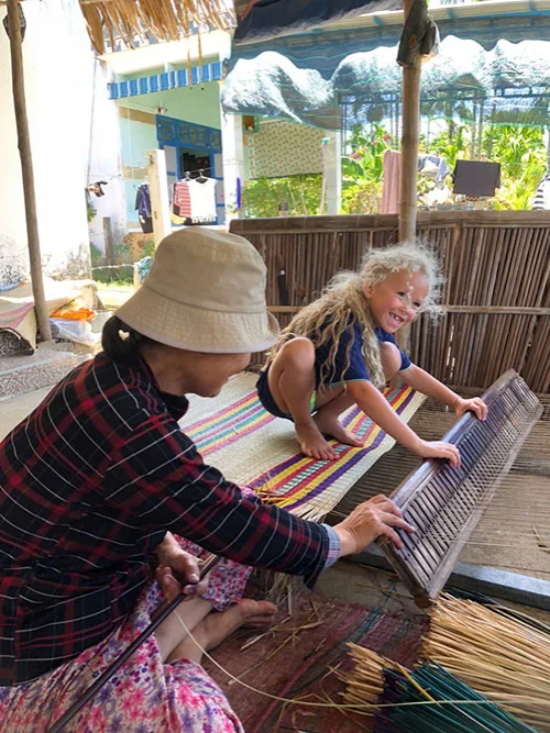 Little girl learning how to weave under the guidance of a local villager