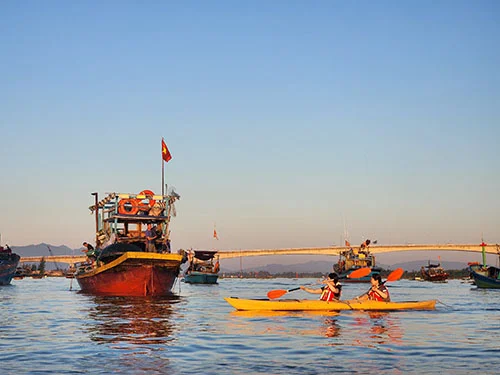 Couple kayaking by fishing boat on the Thu Bon River in Hoian at sunrise