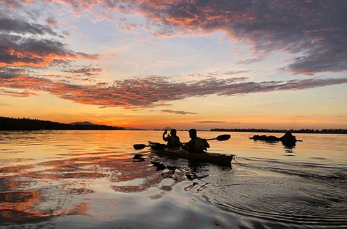 Two people kayaking into the orange sunrise on the Thu Bon River