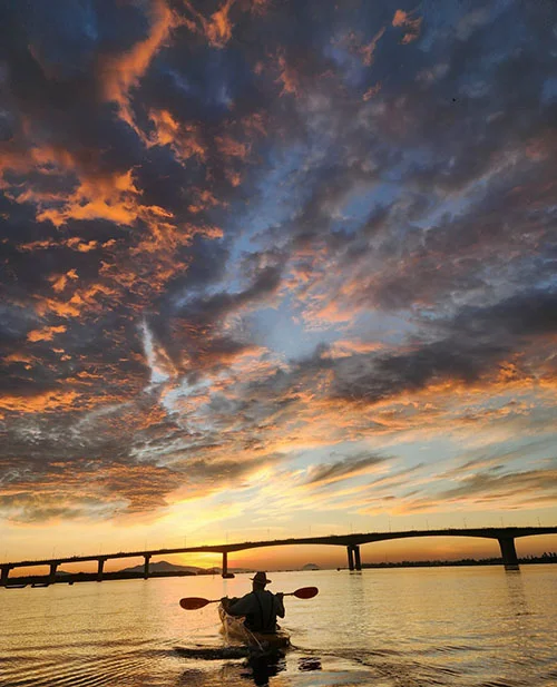 One person kayaking into a colorful as the sun rises upon the Thu Bon River in Hoian