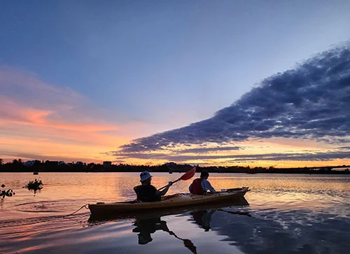 Two travelers in a double kayak taking in the clouds at sunrise