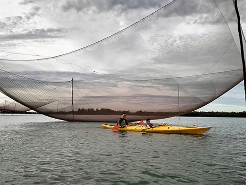 One double kayak with tourist rowing under the elevated fishnet under a cloudy sky